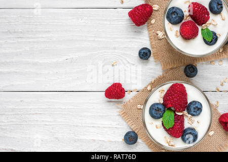 Deux verres de yaourt grec en bonne santé avec les baies fraîches, d'avoine et de menthe sur la table en bois blanc. petit-déjeuner sain. top view with copy space Banque D'Images