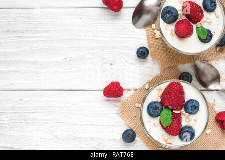 Le yogourt saine avec les baies fraîches et de menthe dans les verres avec des cuillères sur la table en bois blanc. petit-déjeuner sain. top view with copy space Banque D'Images