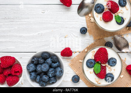 Yaourt à la grecque avec les baies fraîches, d'avoine et de menthe dans les verres avec des cuillères sur la table en bois blanc. petit-déjeuner sain. top view with copy space Banque D'Images