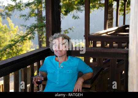 Femme plus détendue assis sur une terrasse extérieure tenant un verre de vin sur un paisible après-midi au plus tard à l'auberge sur le mont Tam, CA, USA Banque D'Images