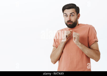 Guy revenir sentiment inquiet et intense femme va frapper. Portrait de peur et nerveux caucasien homme mignon avec flexion barbe poing levé l'arrière près de poitrine sur mur gris Banque D'Images