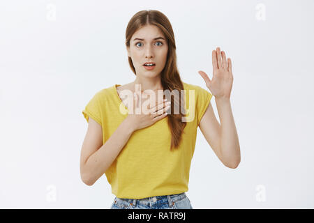 Je jure de dire la vérité. Portrait d'inquiets et nerveux timide cute young girl holding repose sur la poitrine et la part de serment d'être honnête face à juge ou à la Chambre de s'opposer à fond gris Banque D'Images