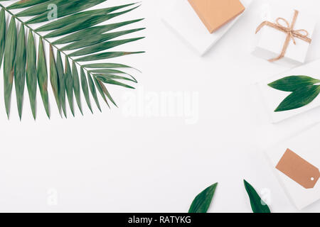 Vue de dessus sur table avec la feuille de palmier et de cadeaux, objets décoratifs mise à plat sur fond blanc avec le centre vide. Banque D'Images