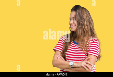 Belle jeune femme brune portant des T-shirt à rayures sur fond isolé à sourire sur le côté avec les bras croisés convaincu et confiant Banque D'Images