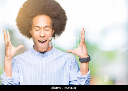 Young african american man with afro hair célébrant mad et fou pour le succès avec les bras levés et les yeux clos des cris excités. Concept gagnant Banque D'Images