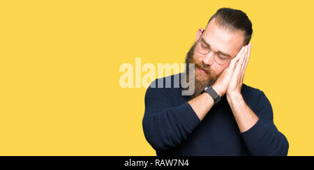 Jeune homme portant des lunettes et Pull col roulé fatigué dormir rêver et posant avec les mains tout en souriant avec les yeux fermés. Banque D'Images