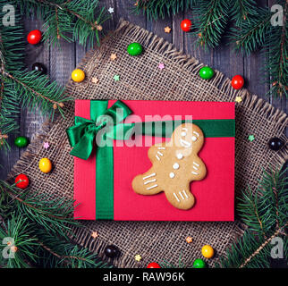 Gingerbread sur le boîte cadeau rouge autour de branches de sapin et de bonbons colorés sur fond de bois Banque D'Images