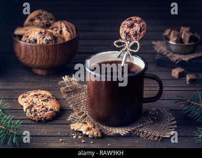 Cuillère décorative à partir de pâte polymère dans la tasse de thé près de cookies au chocolat sur fond de bois Banque D'Images