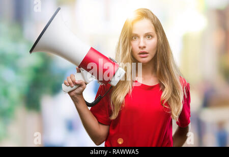 Jeune belle blonde woman yelling through megaphone sur fond isolé en peur avec une surprise de Choc Visage, peur et excité par la peur exp Banque D'Images