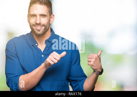 Jeune homme séduisant sur fond isolé en pointant sur l'arrière derrière avec la main et Thumbs up, souriant confiant Banque D'Images