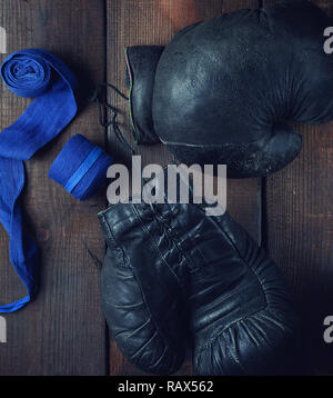 Très ancienne paire de gants de boxe en cuir noir et d'un bandage à la main bleu Banque D'Images