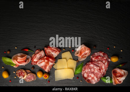 Vue de dessus de l'antipasto au salami, fromages, viande fumée, prosciutto, jambon, olives, les verts sur fond d'ardoise noire Banque D'Images