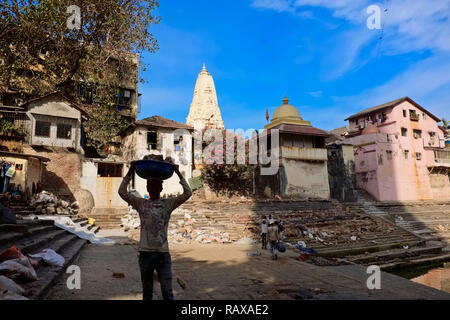 Rénovation d'un travailleur sur Banganga Tank, un temple sacré site dans Mumbai, Inde, transportant des briques sur sa tête, apparaissant presque comme une silhouette Banque D'Images