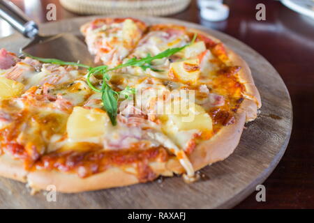 Petites tranches de pizza hawaïenne sur une planche de bois. Banque D'Images