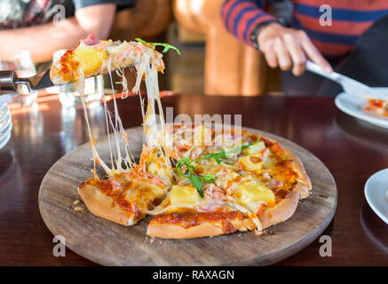 Petites tranches de pizza hawaïenne sur une planche en bois et l'homme en prenant la main de tranches de pizza. Banque D'Images