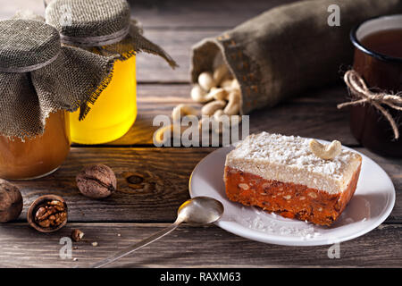 Gâteau végétalien premières à partir de la carotte, noix de cajou et la crème de coco sur le dessus près de pots de miel et de thé mug Banque D'Images