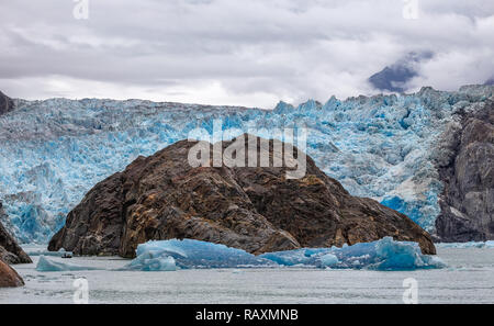 Avis de Sawyer Glacier avec une gigantesque montagne devant elle, un petit bateau naviguant par elle et les icebergs flottant dans l'Alaska's fjord Tracy Arm Banque D'Images