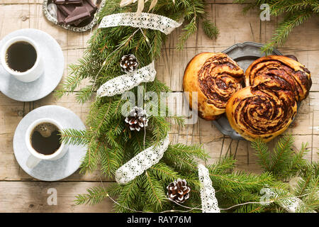 Muffins au chocolat escargot servi avec du café sur l'arrière-plan d'une couronne de branches de sapin et les cônes. Style rustique. Banque D'Images