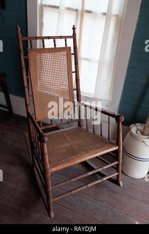 Canne tissé ancien fauteuil à bascule avec baratte sur parquet dans la maison, Texan Historique Chestnut Square Historic Village, McKinney, au Texas. Banque D'Images