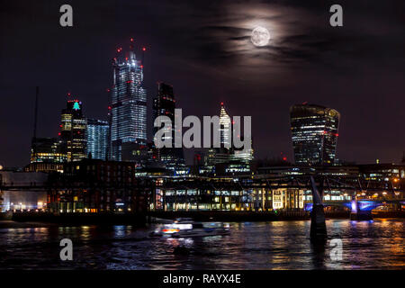 Une très grande lune se lève de derrière les tours de la ville de Londres dans un affichage inhabituel Banque D'Images