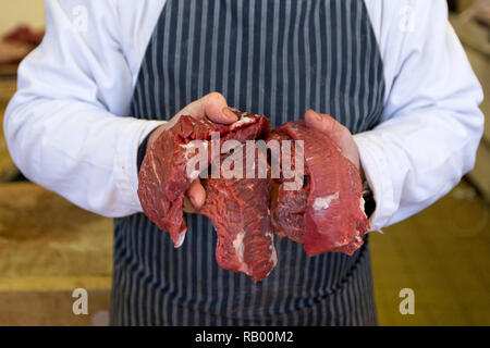 Un boucher pose pour un portrait avec de la viande à vendre dans leur magasin de gros à Smithfield dans la ville de Londres. Févr. 2013. Banque D'Images