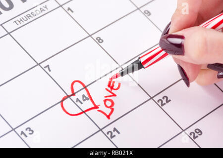 Fille main avec dessin au feutre rouge, forme de coeur et l'écriture mot amour dans Calendrier. L'amour et la Saint-Valentin maison de concept. Close up Banque D'Images