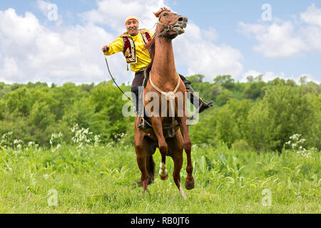 L'homme en costume national Kazakh des manèges et tente d'obtenir son cheval dressé, à Almaty, Kazakhstan. Banque D'Images