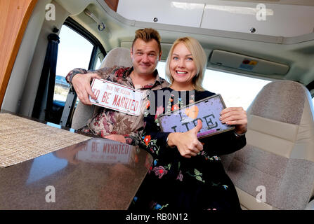L'âge moyen joyeux voyageurs positifs mariés couple assis à l'intérieur de camping-détient montrant la plaque de numéro de style rétro hippy Banque D'Images