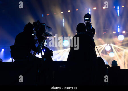 Un groupe de travail de cameramen pendant le concert. Nombre d'événement. Silhouettes d'ouvriers contre l'arrière-plan de faisceaux colorés. Banque D'Images