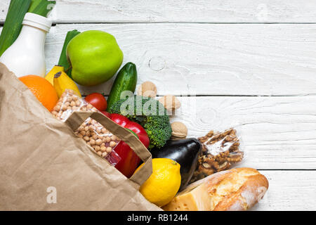 Sac en papier plein de différents aliments végétariens sains on white background. fruits, légumes, noix, du pain et du lait. Vue d'en haut. Mise à plat Banque D'Images