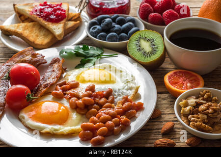 Petit-déjeuner anglais. œuf frit, haricots, tomates, bacon, café et pain grillé aux noix, fruits et baies. close up Banque D'Images