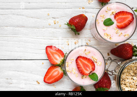 Deux verres de yogourt aux fraises en bonne santé avec les baies fraîches, d'avoine et de menthe sur la table en bois blanc. petit-déjeuner sain. top view with copy space Banque D'Images