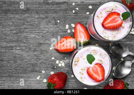 Avec l'avoine yogourt aux fraises et à la menthe dans les verres avec les baies fraîches et des cuillères en bois blanc sur table. petit-déjeuner sain. top view with copy space Banque D'Images