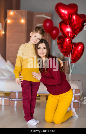 Belle jeune brunette maman mère avec son adolescent beau garçon se tenant et heureux ensemble.Femme en plumes jaunes et rouges plus doux Banque D'Images