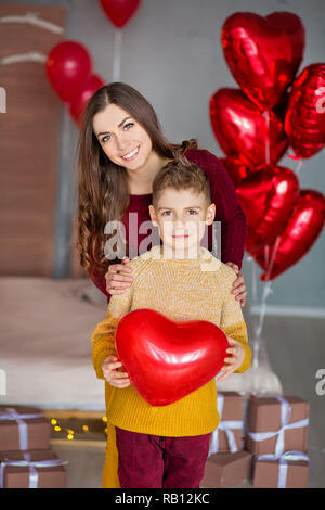 Belle jeune brunette maman mère avec son adolescent beau garçon se tenant et heureux ensemble.Femme en plumes jaunes et rouges plus doux Banque D'Images