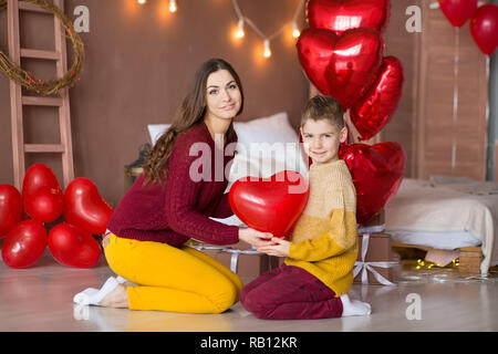 Belle jeune brunette maman mère avec son adolescent beau garçon se tenant et heureux ensemble.Femme en plumes jaunes et rouges plus doux Banque D'Images