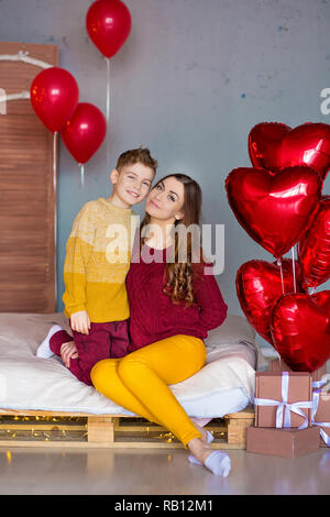 Belle jeune brunette maman mère avec son adolescent beau garçon se tenant et heureux ensemble.Femme en plumes jaunes et rouges plus doux Banque D'Images