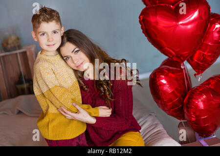 Belle jeune brunette maman mère avec son adolescent beau garçon se tenant et heureux ensemble.Femme en plumes jaunes et rouges plus doux Banque D'Images