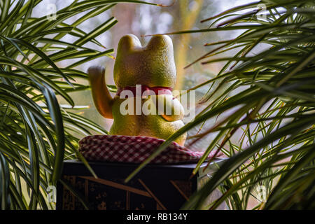 Close up of a Chinese golden fortune cat (maneki neko) sur un rebord de fenêtre entre les plantes Banque D'Images