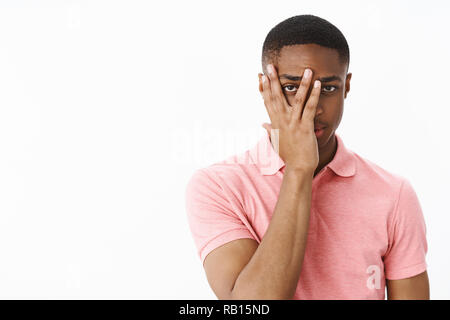 Guy regarder caméra dans les doigts sur la face à de sérieux et intéressés ce qui se passait, ce qui pose en curieux polo rose anticiper pour spectacle debout sur fond gris Banque D'Images