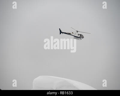 Hélicoptère Blanc survole les montagnes enneigées sur un jour nuageux. Banque D'Images