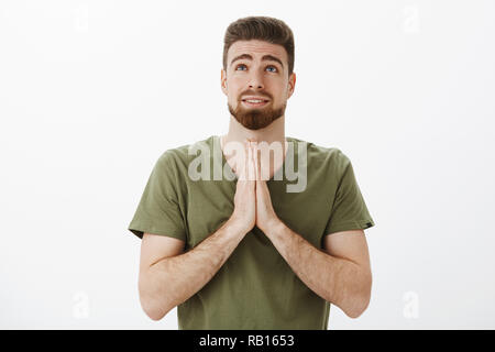 Tourné à l'intérieur de petit ami mignon priant Dieu jusqu'à la holding comme paumes ensemble à prier sur la poitrine, souhaite anticiper, espérons-supplicating rêve sur fond blanc, la mendicité Banque D'Images