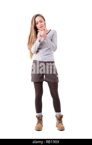 Femme spontanée franche dans de vêtements d'allumer une cigarette avec briquet. Corps plein isolé sur fond blanc. Banque D'Images