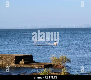 Un pêcheur debout jusqu'à l'ajout d'un filet de pêche dans le Lac Nicaragua avec d'énormes éoliennes dans l'arrière-plan Banque D'Images