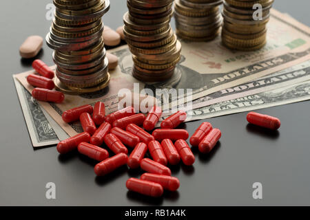 Comprimés ou Capsules rouges contre des dollars et des piles de pièces de monnaie sur le fond sombre. Concept de traitement coûteux Banque D'Images