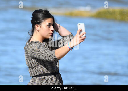 Jeune femme, adolescent ou début 20s, photographie selfies sur un smartphone sur une plage. Banque D'Images