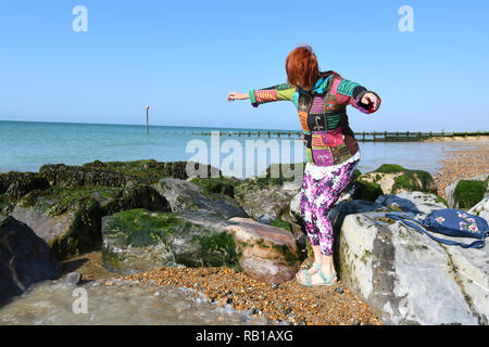 Bien habillé à la mode jeune à hauts femme marche sur une plage de galets sur les cailloux et les rochers dans le Royaume-Uni. Banque D'Images