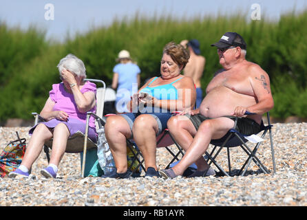 Groupe de gens assis au soleil sur la plage sur une chaude journée d'été au cours de la canicule de 2018 au Royaume-Uni. Banque D'Images