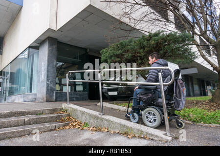 Homme en fauteuil roulant à l'aide d'une rampe à côté d'escaliers Banque D'Images