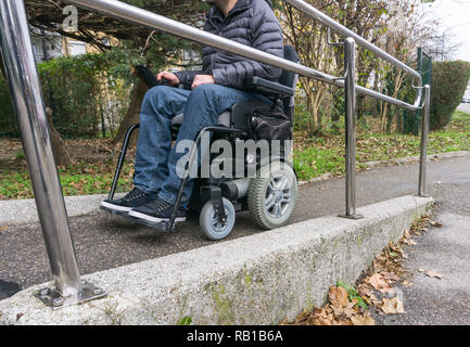 Homme en fauteuil roulant à l'aide d'une rampe à côté d'escaliers Banque D'Images